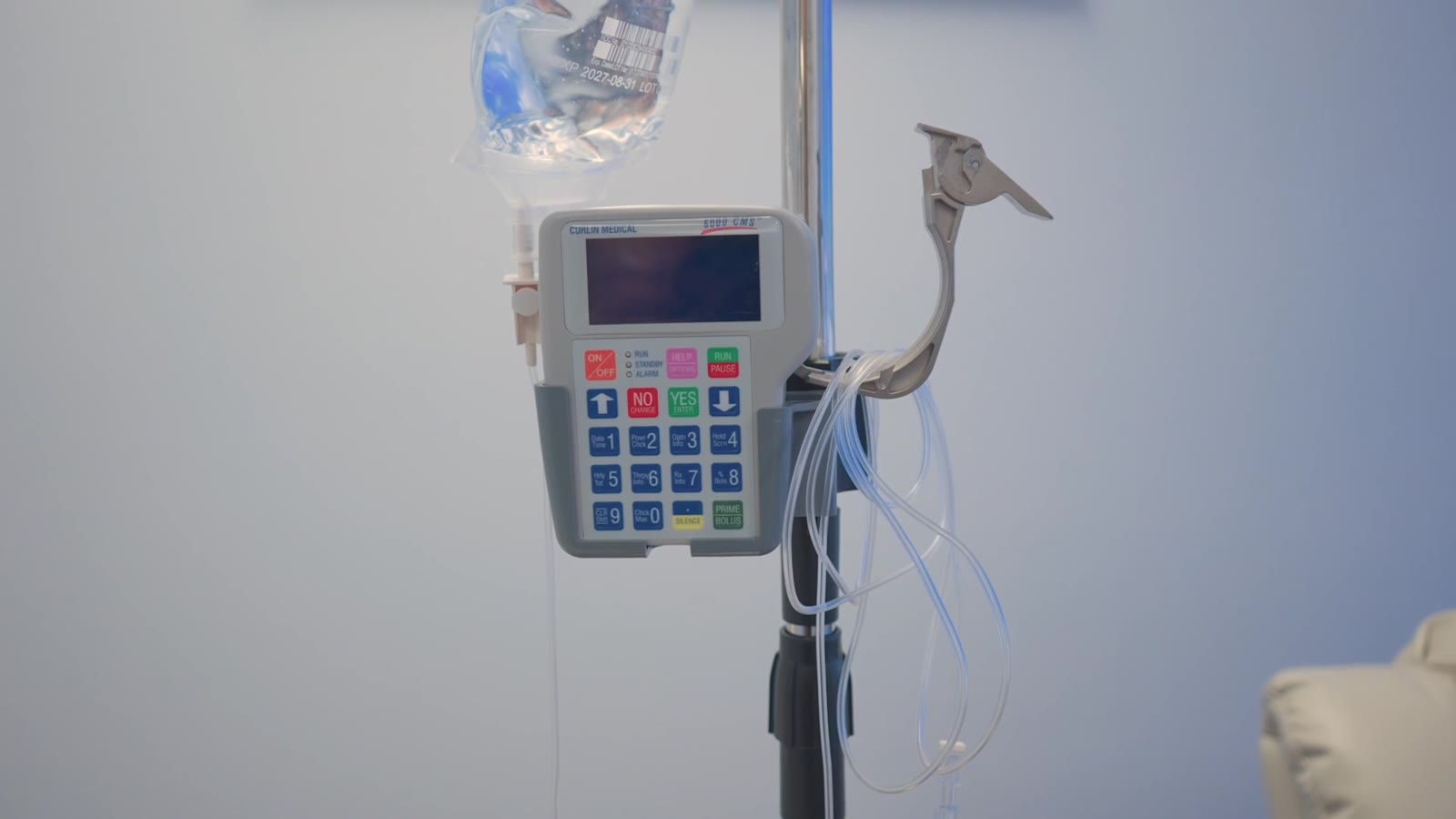An infusion pump on its stand beside a recliner